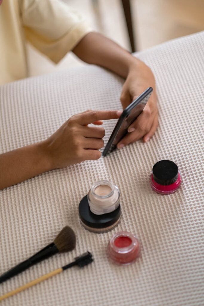Person Using Smartphone Beside Some Beauty Products On Table